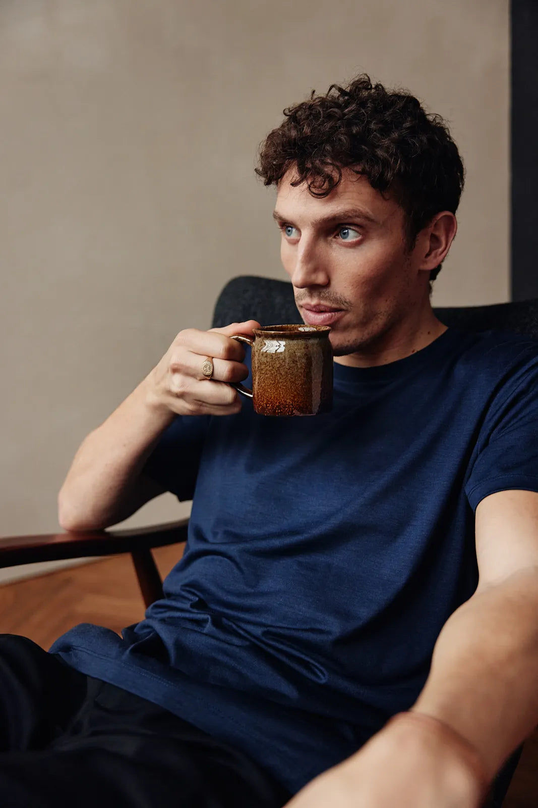 Lifestyle shot of a men's merino wool T-shirt in dark navy. The model drinks a coffee.