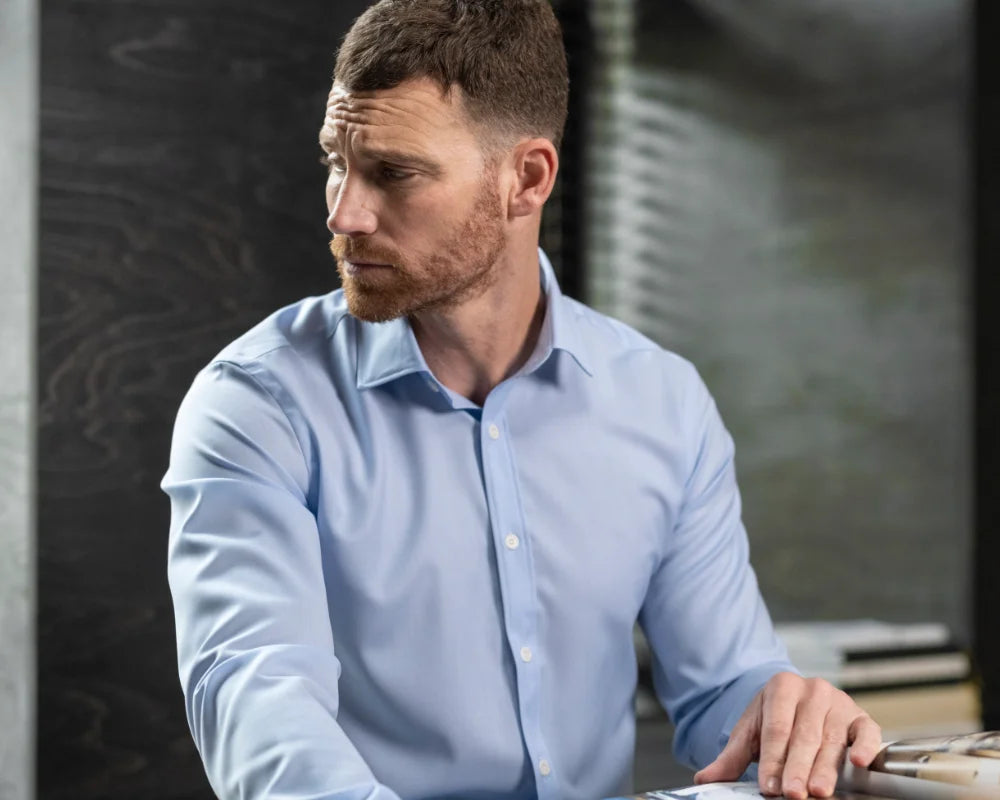 Man in a light blue merino shirt sitting at a desk with a blurred background