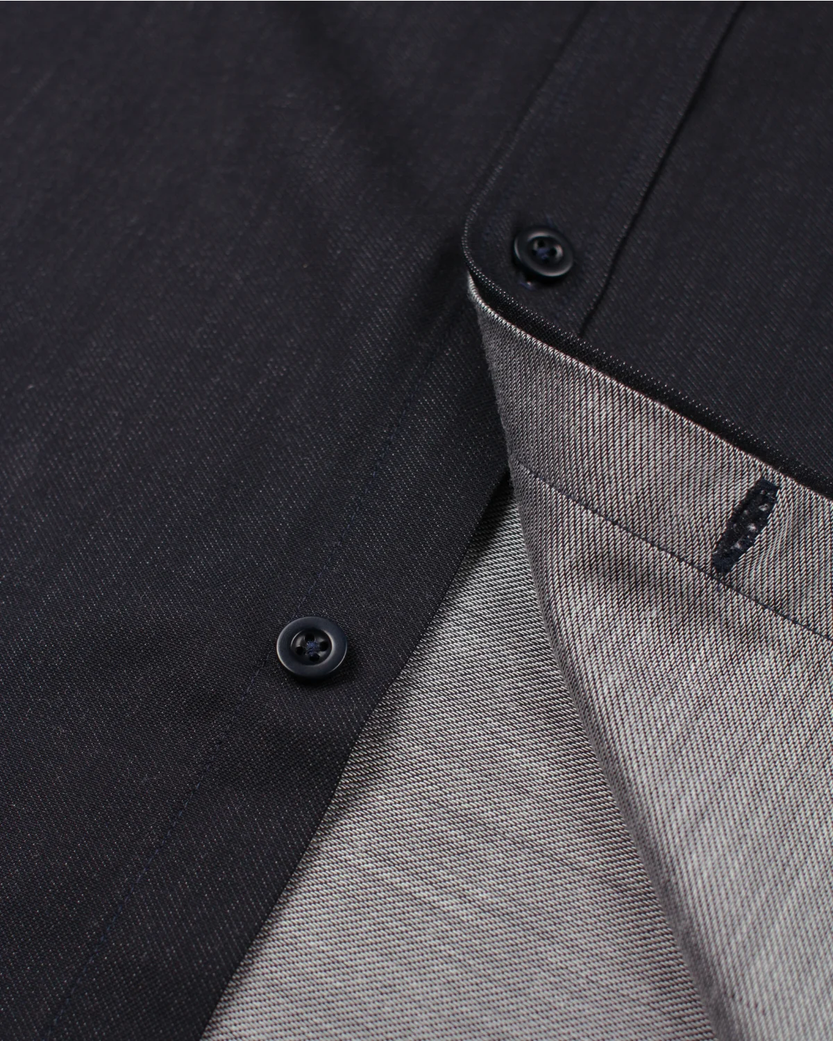 Close-up detail of a dark navy merino wool woven shirt fabric showing the front fabric, navy buttons, and the lighter gray backside of the fabric