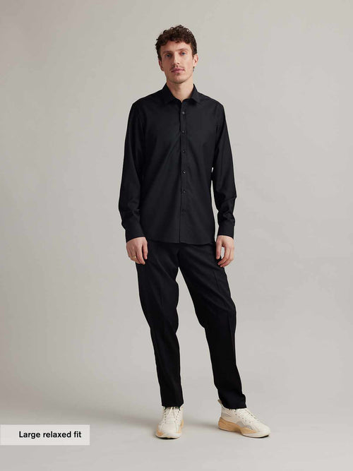 Man wears a black merino wool shirt with long sleeves, classic collar and black buttons in relaxed fit