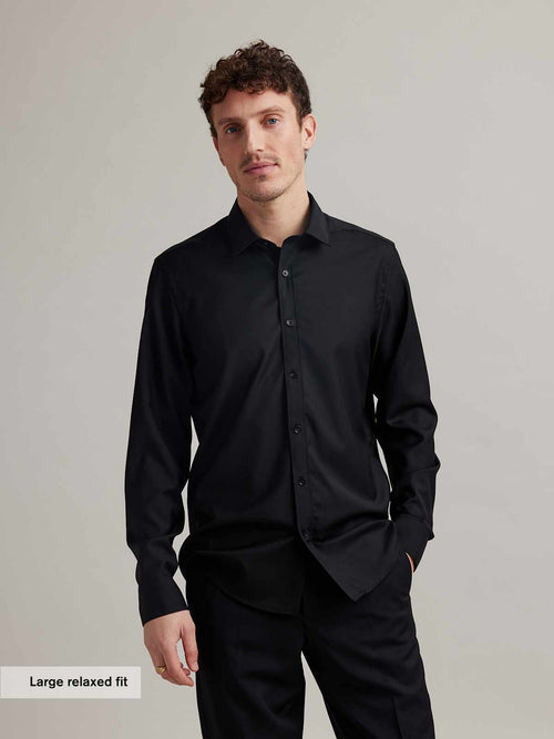 Man wears a black merino wool shirt with long sleeves, classic collar and black buttons in relaxed fit