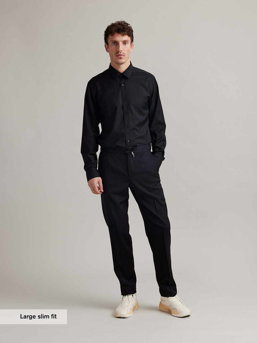 Man wears a black merino wool shirt with long sleeves, classic collar and black buttons in slim fit