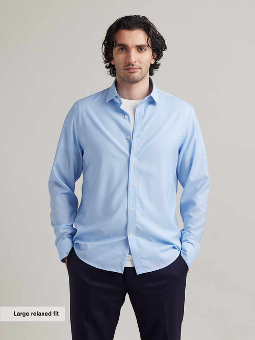 man wears light blue merino wool shirt with white merino T-shirt underneath on navy blue pants.
