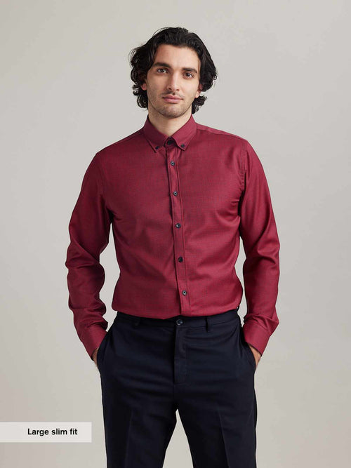 Man wears merino wool shirt with button down collar in red navy mini gingham pattern tucked in a navy blue trousers