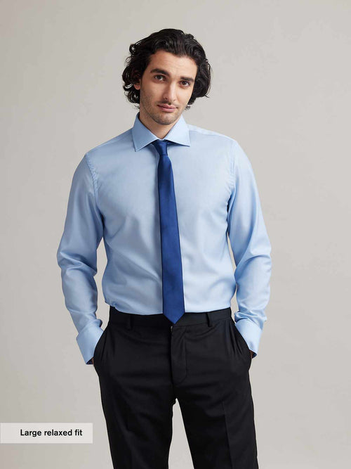 Man wears a light blue formal merino wool shirt from Wolk with English spread collar and blue tie on black suit trousers