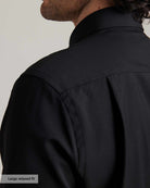 Close-up of a man wearing a black merino wool shirt. It shows the shoulder detail, the back pleat of the relaxed fit and the collar. 