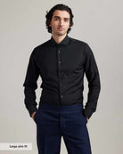 Man wearing a black merino wool shirt from Wolk and navy pants against a plain background