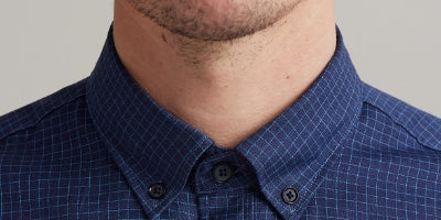 Close-up of a person wearing a blue checkered shirt with button down collar against a neutral background