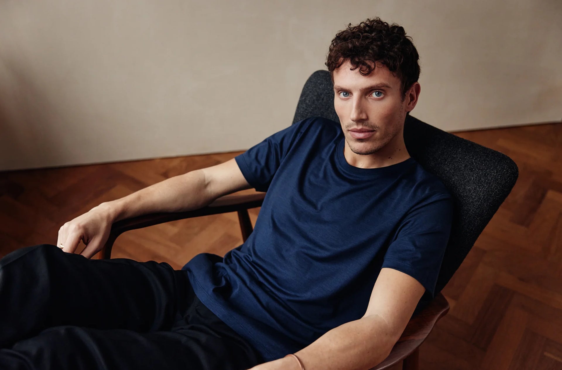 Man sitting in a chair wearing a blue merino wool T-shirt against a neutral background