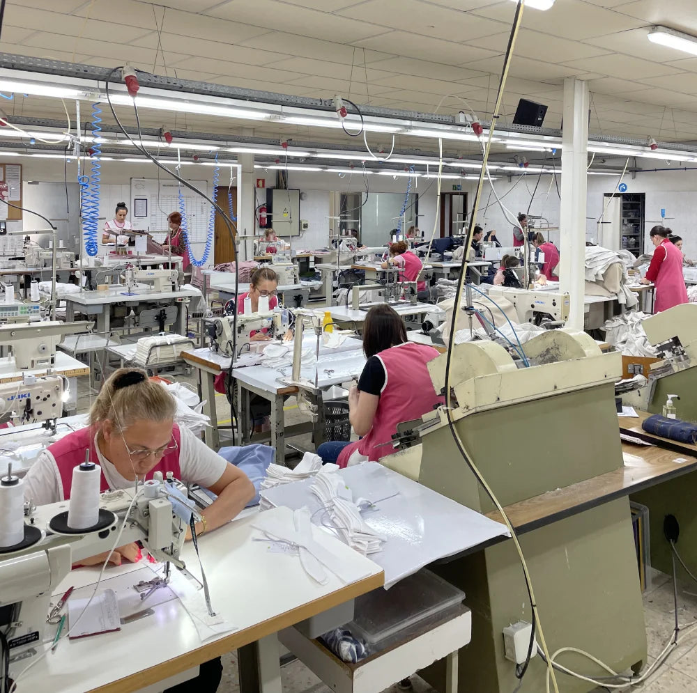Factory floor with workers operating sewing machines in a busy production setting.