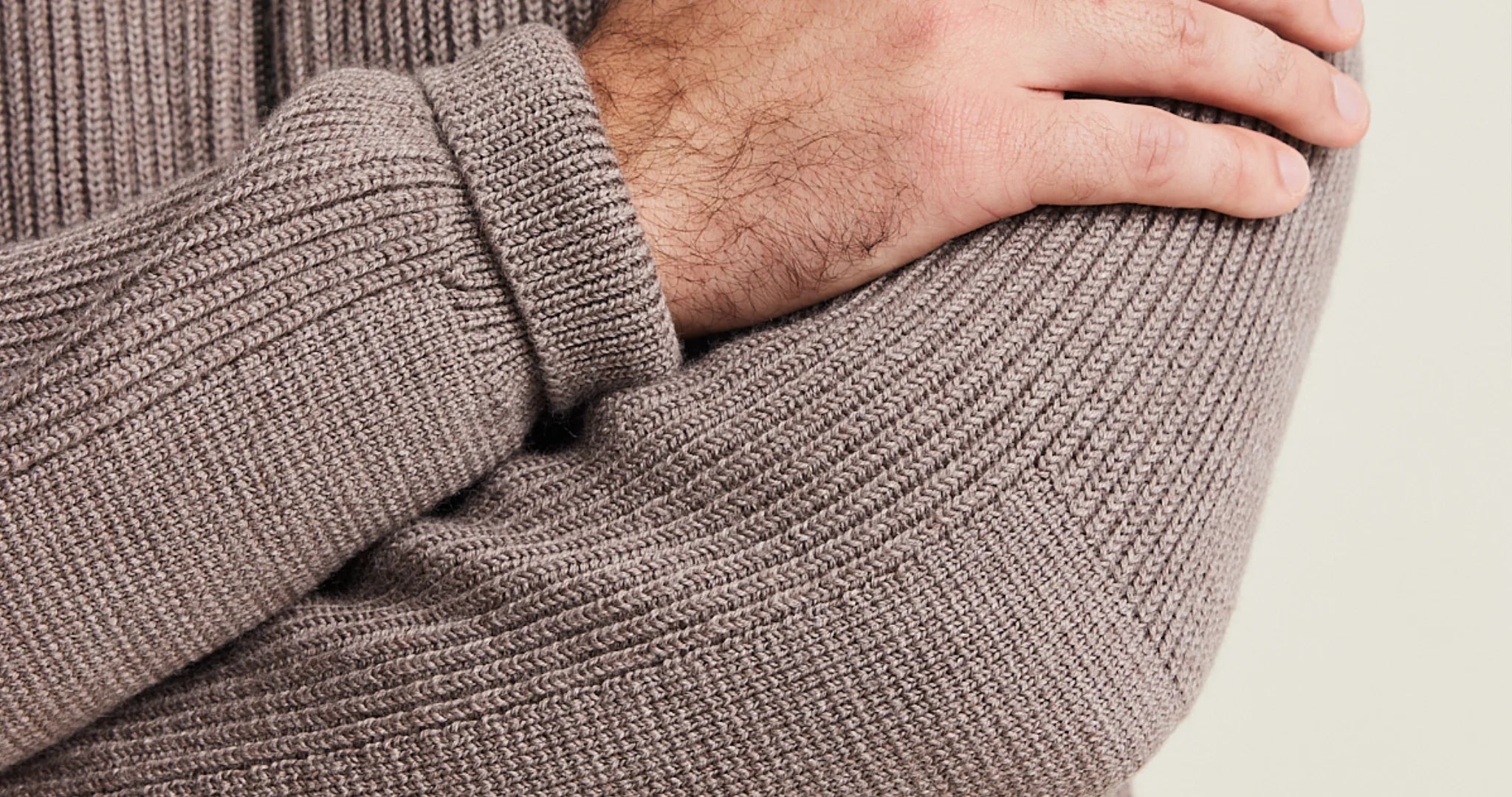 Close-up of a person wearing a brown knitted merino wool sweater with a neutral background