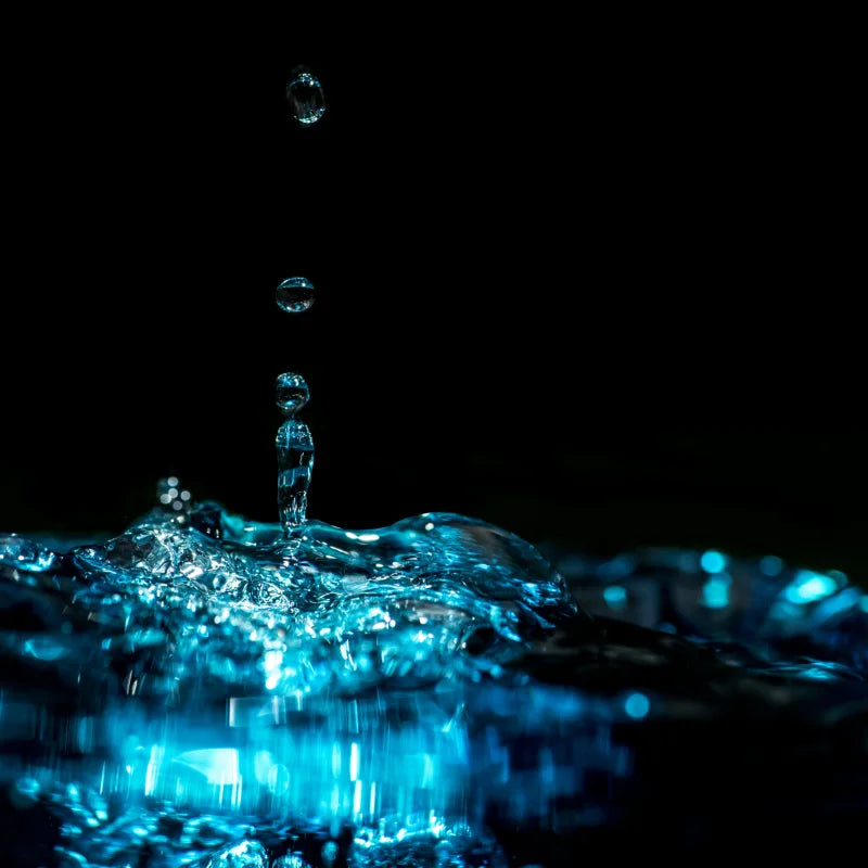 Water droplet creating ripples on water surface with black background