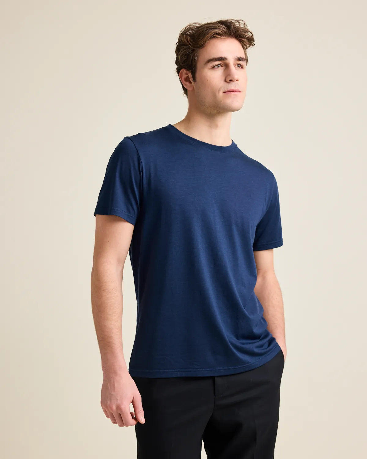 Man wearing a navy merinowool Tshirt from Wolk on black trousers in a studio setting