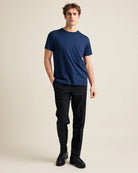 Man wearing a navy t-shirt and black pants on a beige background