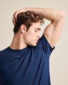 man wearing a navy merino tshirt and smelling the armpit to check the freshness