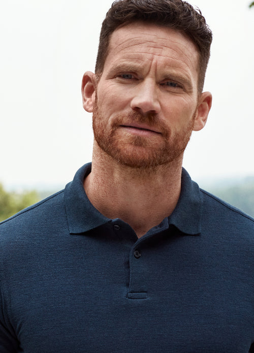 Close up of man wearing a merino wool polo in navy blue color with rub collar and corozo buttons
