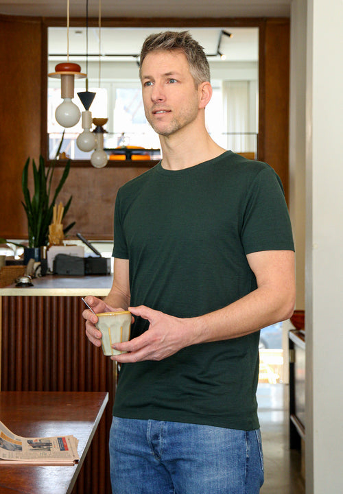 Man wears a short sleeve merino wool Tshirt in dark green with round neck in 170 g/sqm weight